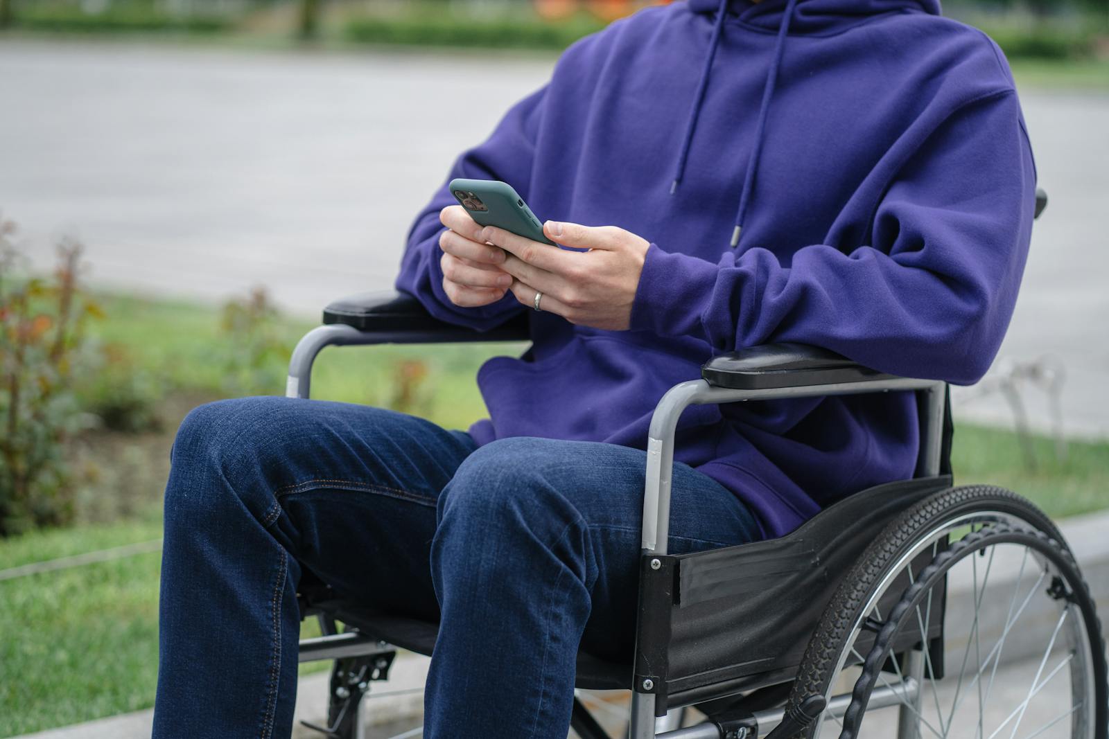 Person in Purple Hoodie and Blue Denim Jeans Sitting on Black Wheel Chair